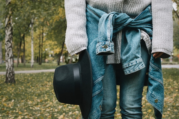 Retrato sin rostro de joven mujer en suéter y chaqueta vaquera con sombrero negro en sus manos