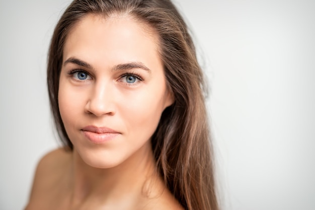 Foto retrato de rostro de mujer caucásica joven con maquillaje natural y extensiones de pestañas mirando a cámara sobre fondo blanco.