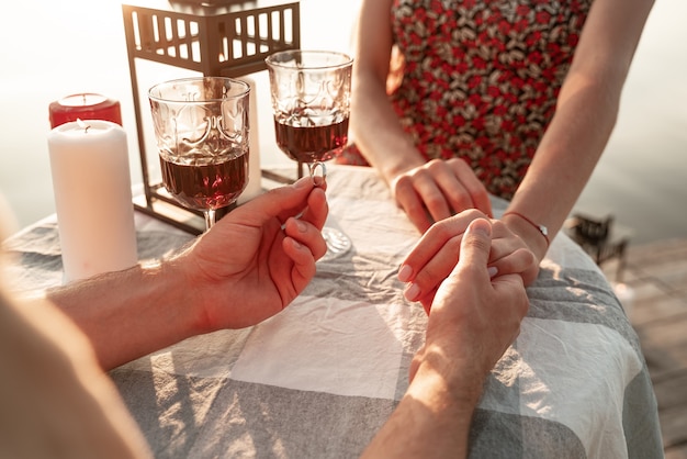 Retrato sin rostro de pareja pasar tiempo juntos bebiendo vino afuera: hombre sosteniendo la mano de su novia y el anillo de compromiso haciendo propuesta de matrimonio. Hermosa ceremonia de propuesta, el amor está en el aire.