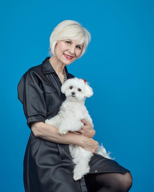 Foto retrato de una rubia adulta con un pequeño perro faldero maltés sobre un fondo azul.