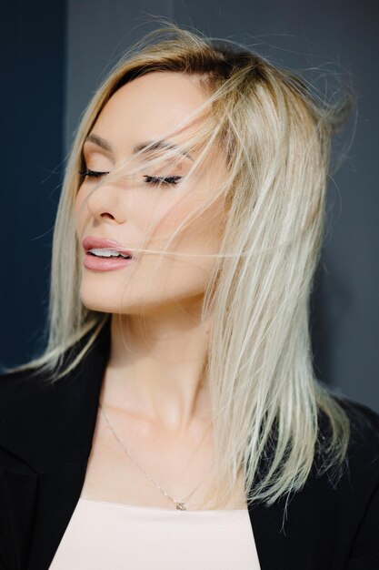 Retrato de rubia hermosa joven elegante mujer con el cabello revoloteando en la pared gris de la ciudad