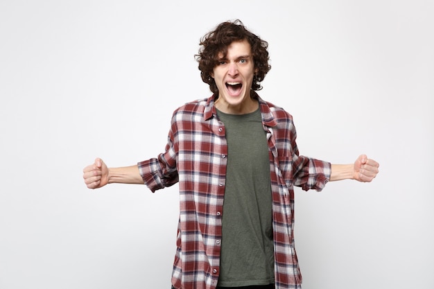 Retrato de salvaje joven gritando en ropa casual extendiendo las manos, apretando los puños aislados sobre fondo de pared blanca en estudio. Personas sinceras emociones, concepto de estilo de vida. Simulacros de espacio de copia.