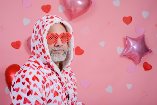 Retrato de San Valentín de un hombre de cabello gris con gafas en forma de corazón y túnica de baño con corazones rojos