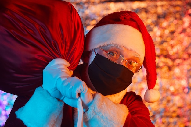 Retrato de Santa Claus en máscara protectora con gran bolsa pesada para la fiesta de Navidad