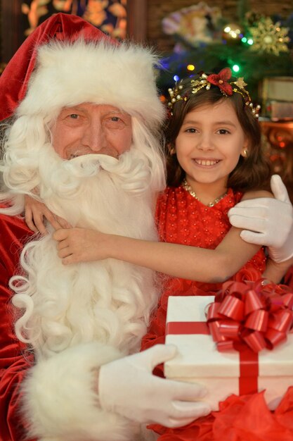 Retrato de Santa Claus y niña feliz con regalo por árbol de Navidad