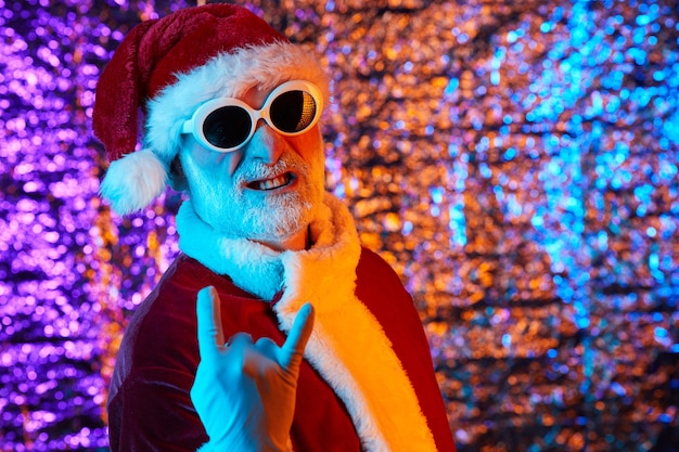 Retrato de Santa Claus en traje rojo y gafas de sol posando sobre el fondo brillante