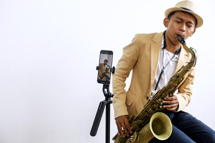 Foto retrato de un saxofonista tocando una música mientras graba un vlog usando un teléfono inteligente en un estudio de música