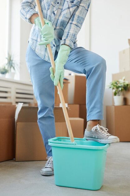 Retrato de sección baja vertical de alegre joven limpiando casa o apartamento nuevo mientras se muda