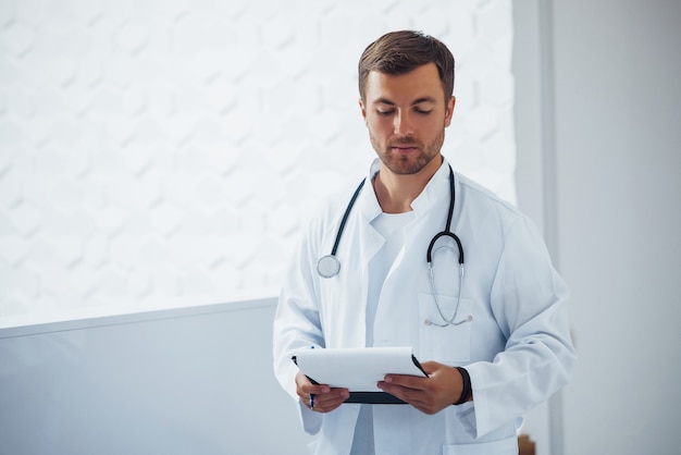 Retrato de seguro médico masculino con estetoscopio y documentos que se encuentra en la clínica.