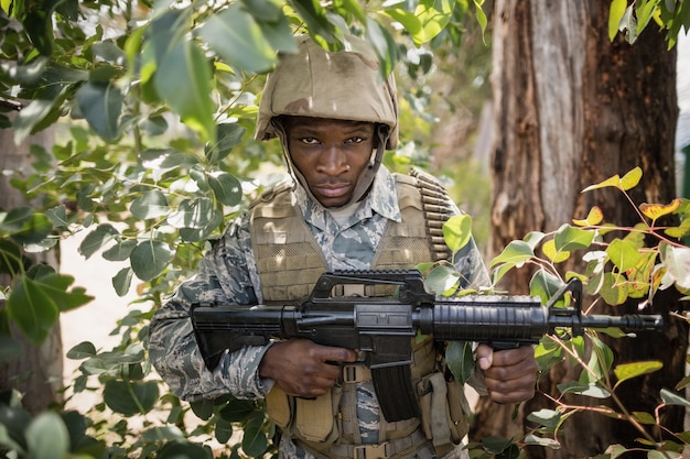 Retrato de seguro soldado militar custodiando con un rifle en el campo de entrenamiento