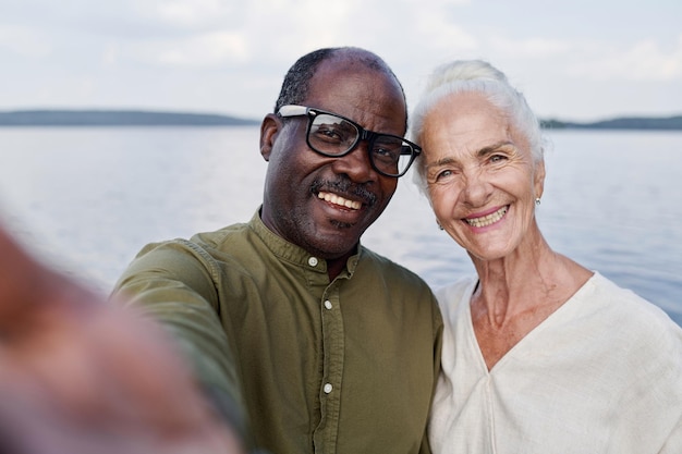 Retrato selfie de casal sênior feliz sorrindo para a câmera enquanto estava ao ar livre contra o lago