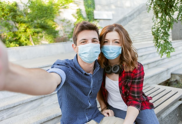 Foto retrato selfie de una joven pareja amorosa con máscaras protectoras médicas al aire libre. protección antivirus, pandemia de covid-19