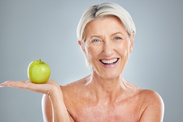 Retrato sênior e mulher com maçã no estúdio para saúde, bem-estar e dieta em uma maquete de fundo cinza Face fruta e modelo maduro sorriso feliz e relaxamento estilo de vida saudável desintoxicação e nutrição