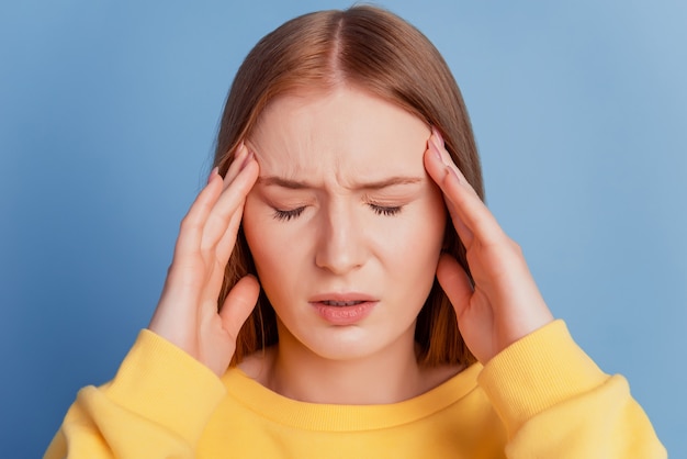 Retrato de señora enferma preocupada cansado manos templos sufren dolor de cabeza sobre fondo azul.