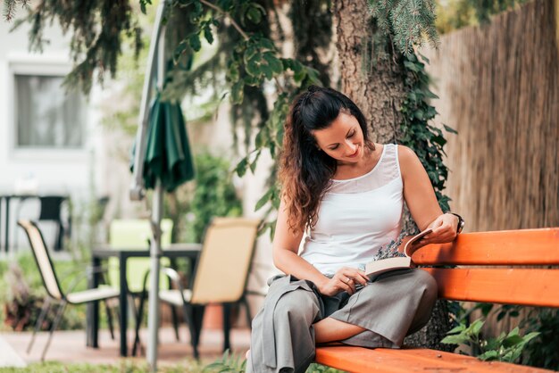 Retrato de una señora que lee un libro al aire libre.