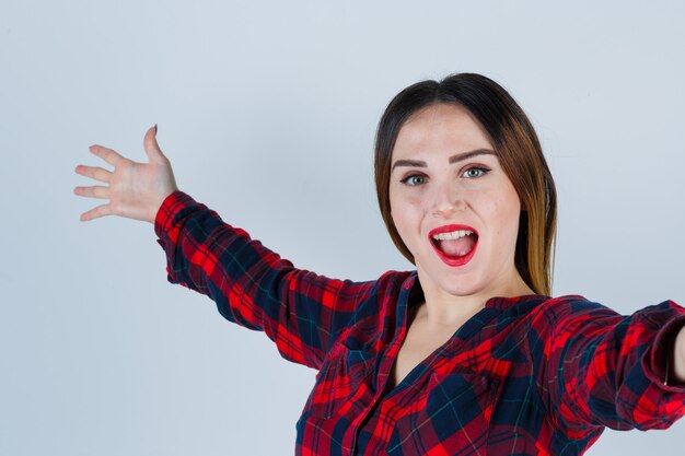 Retrato de señorita abriendo los brazos para abrazar en camisa a cuadros y mirando alegre vista frontal