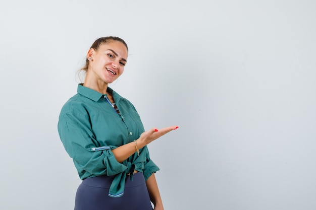 Retrato de señorita mostrando algo en el espacio de la copia. Camisa verde y mirando alegre vista frontal