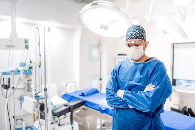 Retrato sério de cirurgião masculino na sala de cirurgia com luzes de cirurgia acesas e dispositivos médicos Detalhes modernos do hospital