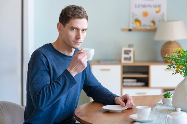 Retrato de serio triste malestar chico guapo joven hermoso está bebiendo té de café de blanco