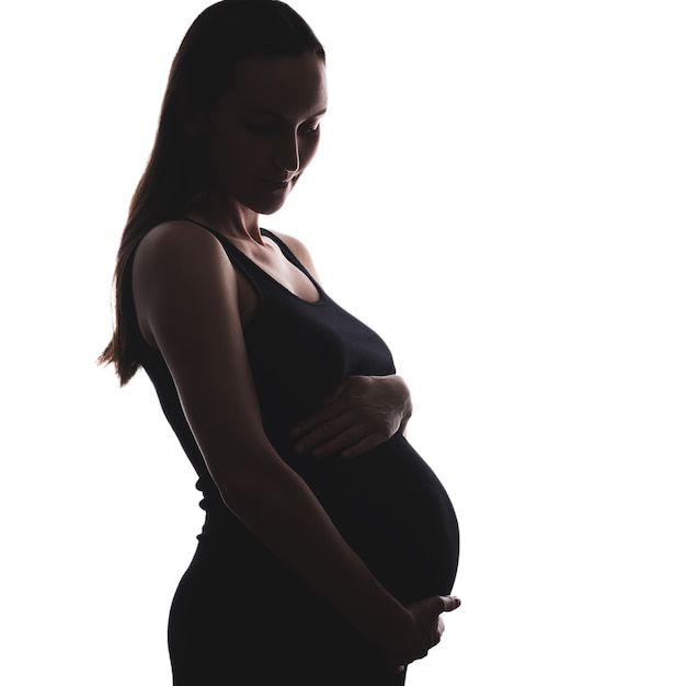 Retrato de silueta de mujer embarazada en vestido negro con la mano en el vientre sobre fondo blanco.