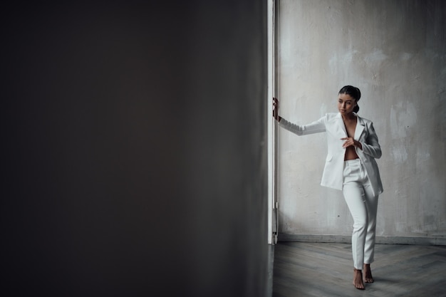 Retrato de una sincera auténtica elegante y sexy modelo de raza mixta posando en traje de pantalón blanco con sujetador