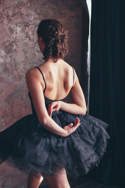 Retrato sincero de bailarina bailarina de costas em vestido preto posando no estúdio loft