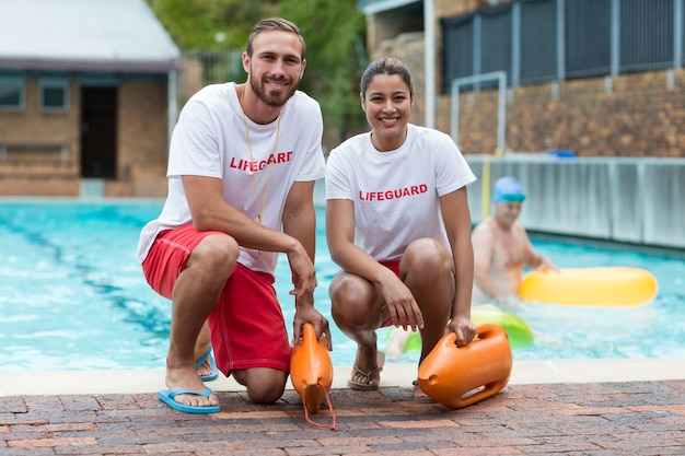 Retrato de socorristas masculinos y femeninos sosteniendo latas de rescate junto a la piscina