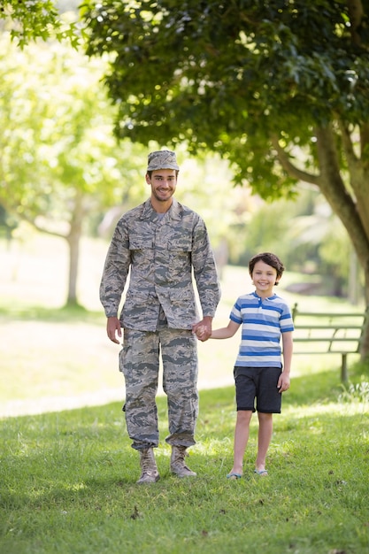 Retrato del soldado del ejército tomados de la mano de su hijo en el parque
