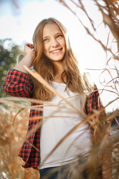 Retrato soleado al aire libre vertical de estilo de vida de una joven adolescente sonriente mirando fuera de la cámara