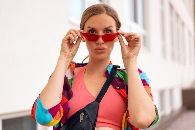 Foto retrato soleado de verano de una mujer rubia bonita con ropa informal brillante y gafas de sol haciendo muecas.