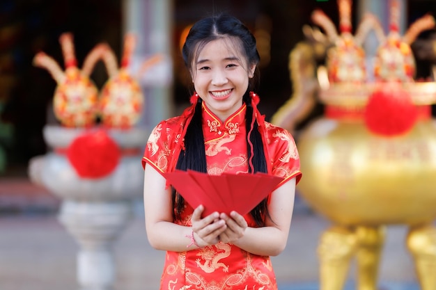 Retrato sonríe a una joven asiática con un vestido rojo de cheongsam sosteniendo sobres rojos decorados para el festival de año nuevo chino celebrando la cultura de China en el santuario chino Lugares públicos en Tailandia