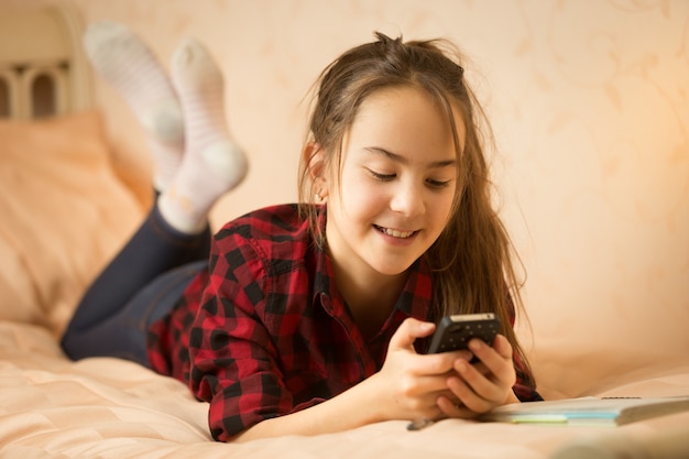 Retrato de sonriente adolescente ling en la cama y con smartphone