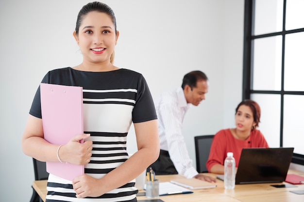 Retrato de sonriente bastante empresaria India de pie en la oficina con la carpeta de documentos en las manos