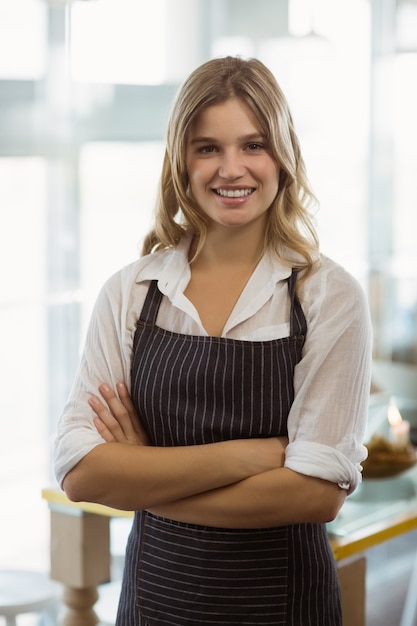 Retrato de sonriente camarera de pie con los brazos cruzados