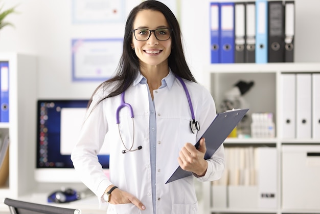 Retrato de sonriente doctora en bata blanca en consultorio médico