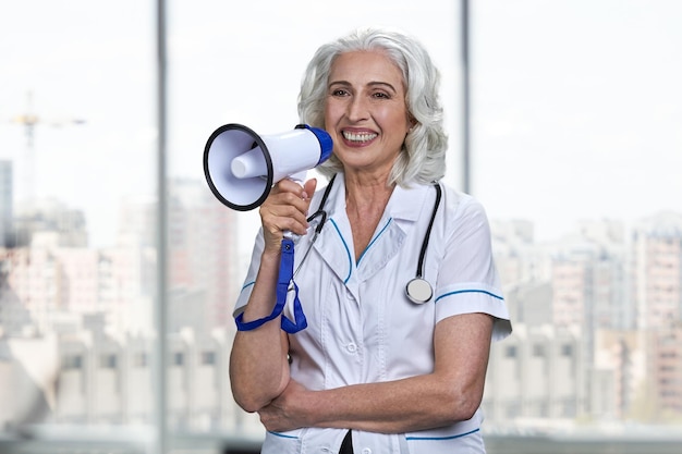 Retrato de sonriente doctora senior hablando por megáfono.