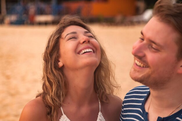 Retrato sonriente encantadora pareja divirtiéndose en la playa de arena tropical en el fondo de palmeras Hombre y mujer felices riendo felicidad