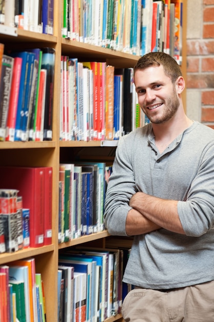 Retrato de un sonriente estudiante masculino apoyado en un estante