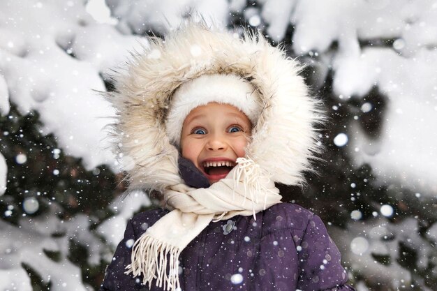 Retrato sonriente feliz de invierno de cerca la cara del niño de la sonrisa alegre emocional en la capucha de piel
