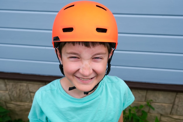 Foto retrato de un sonriente feliz muchacho caucásico adolescente con casco deportivo naranja, aprendiendo a andar en bicicleta o patineta en verano, seguridad y protección durante la actividad infantil al aire libre.