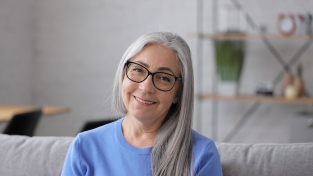 Foto retrato de sonriente hermosa anciana canosa mirando a cámara.