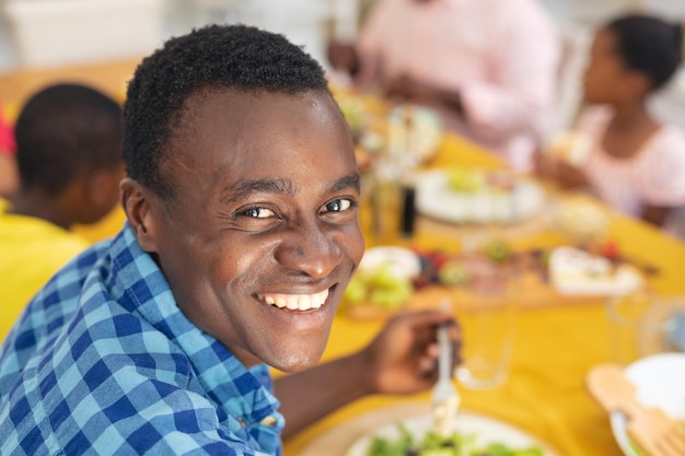 Retrato de un sonriente hombre afroamericano de mediana edad almorzando con su familia el día de acción de gracias. inalterado, familia, comida, convivencia, culturas y concepto de vacaciones.