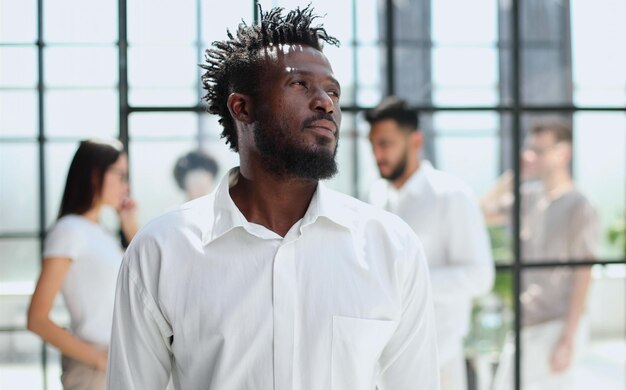 Retrato de sonriente hombre de negocios afroamericano con ejecutivos que trabajan en segundo plano.