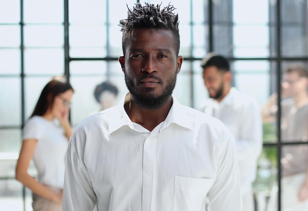 Retrato de sonriente hombre de negocios afroamericano con ejecutivos que trabajan en segundo plano.