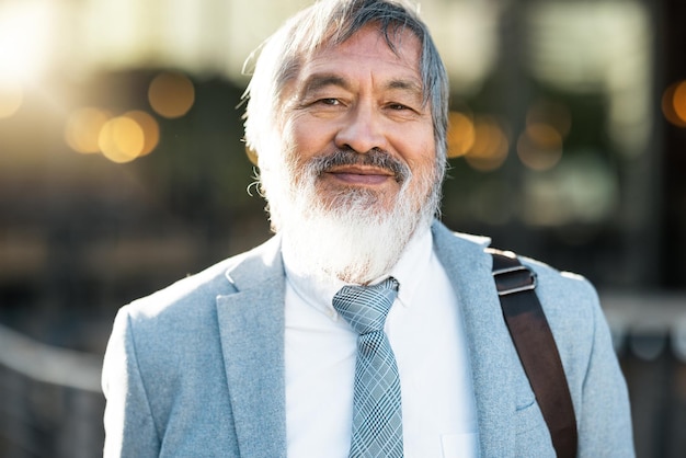 Retrato sonriente y hombre de negocios asiático de alto nivel parado al aire libre junto a su edificio de oficinas en la ciudad Cara feliz y gerente anciano profesional de Asia con una mentalidad positiva en una ciudad urbana