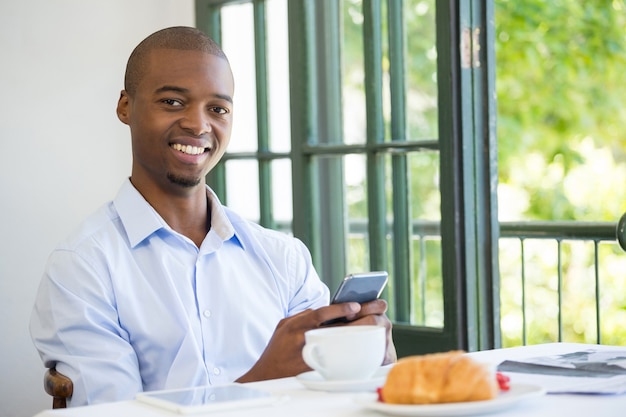 Retrato, de, sonriente, hombre de negocios, tenencia, teléfono móvil, en, restaurante