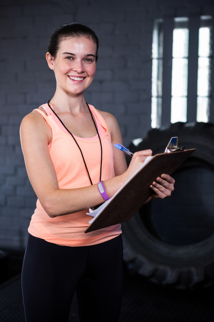 Foto retrato de sonriente instructor de fitness femenino escribiendo en portapapeles