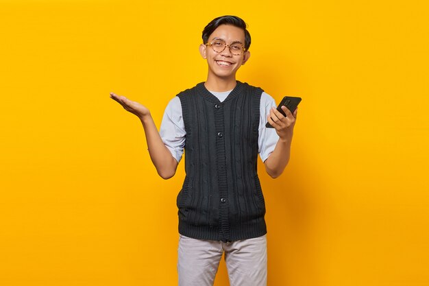 Retrato de sonriente joven guapo mostrando copia espacio en la palma y sosteniendo el teléfono inteligente