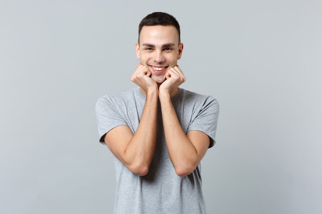 Retrato de sonriente joven guapo en ropa casual de pie, apretando los puños cerca de la barbilla