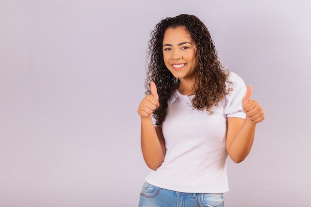 Retrato de sonriente joven hermosa niña afro pulgar hacia arriba. Chica brasileña.